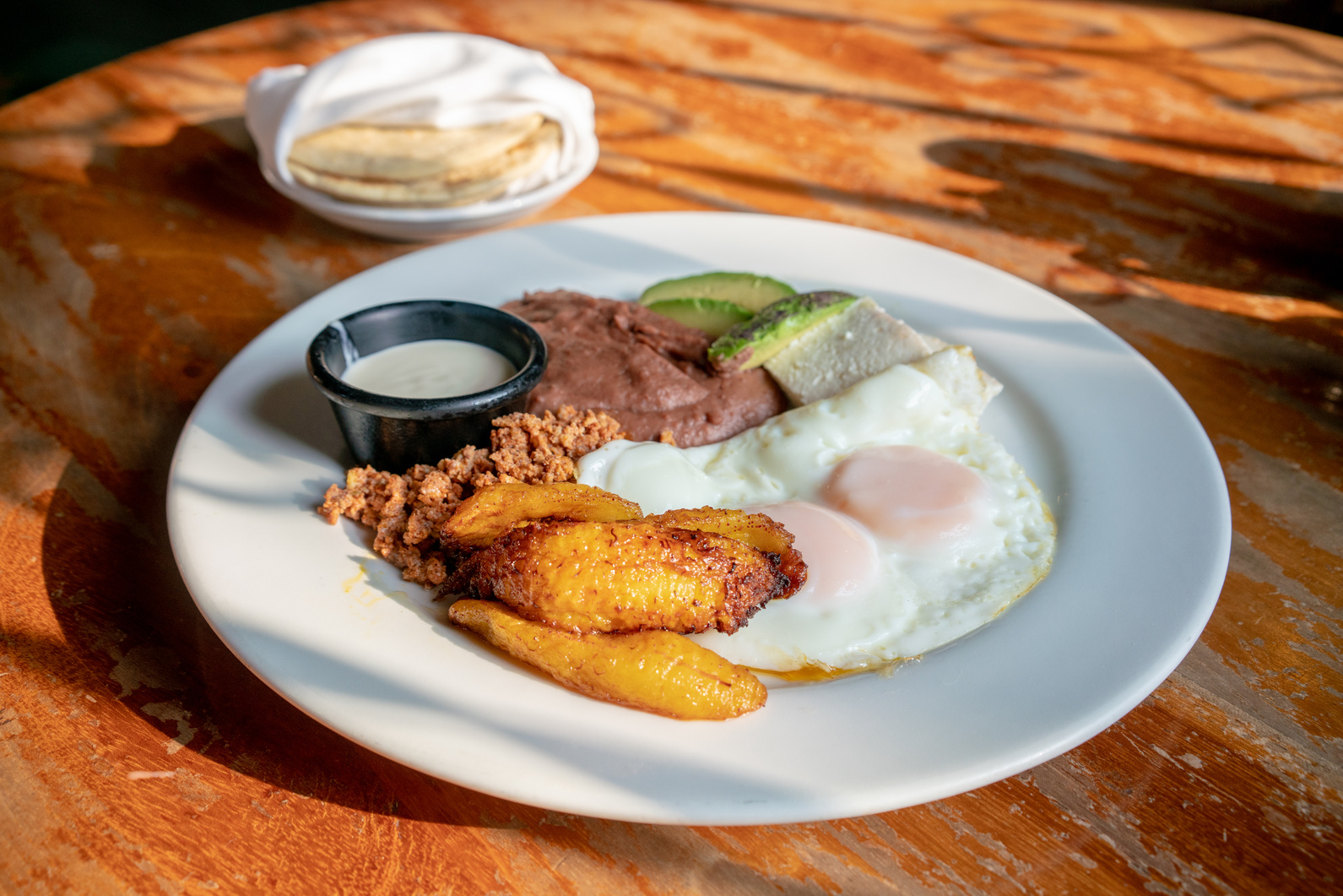 Traditional Honduran Breakfast with chorizo, fried eggs and plantains on a wooden table